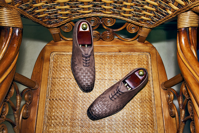 Prawidła do butów na zdjęciu przedstawione są brązowe buty z prawidłami na wiklinowym fotelu